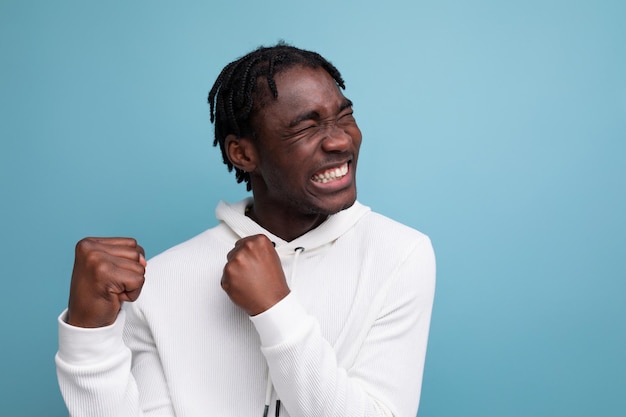 Retrato de un hombre optimista con rastas en una sudadera con capucha blanca sobre un fondo azul.