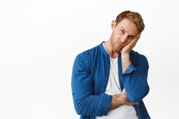 Retrato de hombre pelirrojo aburrido con la cara exhausta en la mano mirando molesto por algo aburrido o poco interesante que se muestra reacio contra el fondo blanco