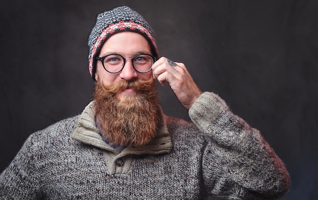 Retrato de un hombre pelirrojo barbudo con anteojos vestido con un suéter de lana y un sombrero.