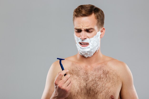 Retrato de un hombre pensativo antes de afeitarse sobre pared gris