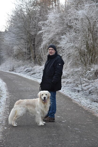 Foto retrato de un hombre con un perro de pie en la carretera durante el invierno