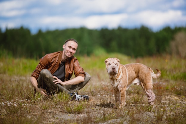 Retrato de un hombre y un perro de raza Shar Pei sentado en el suelo en un prado