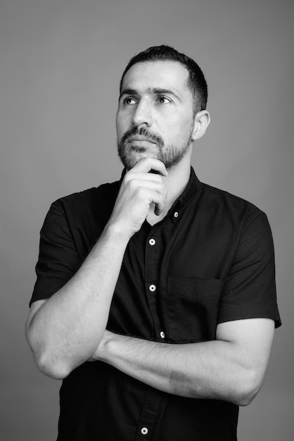 Retrato de hombre persa barbudo guapo con camisa negra sobre gris en blanco y negro