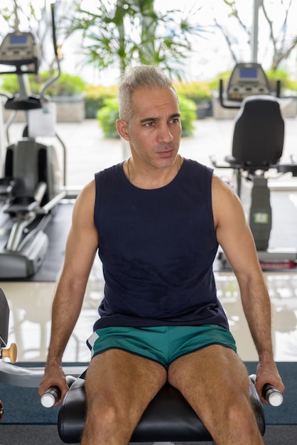 Retrato de hombre persa guapo maduro con cabello gris haciendo ejercicio en el gimnasio