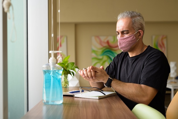 Retrato de hombre persa con máscara para protegerse del brote del virus corona en la biblioteca dentro del edificio moderno