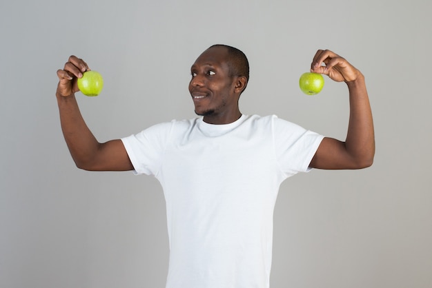 Retrato de hombre de piel oscura con camiseta blanca mirando manzanas verdes en la pared gris