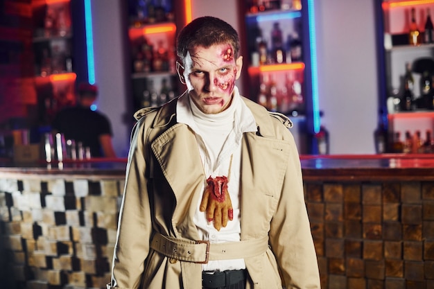 Retrato de hombre que está en la fiesta temática de halloween con disfraz y maquillaje de zombie.
