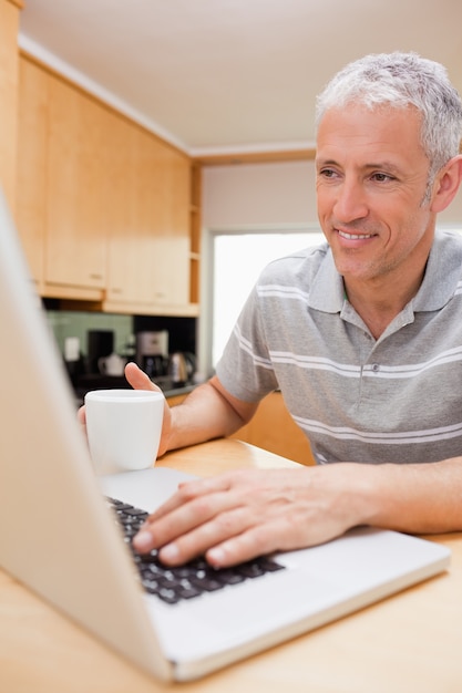 Retrato de un hombre que usa una computadora portátil mientras que bebe el café