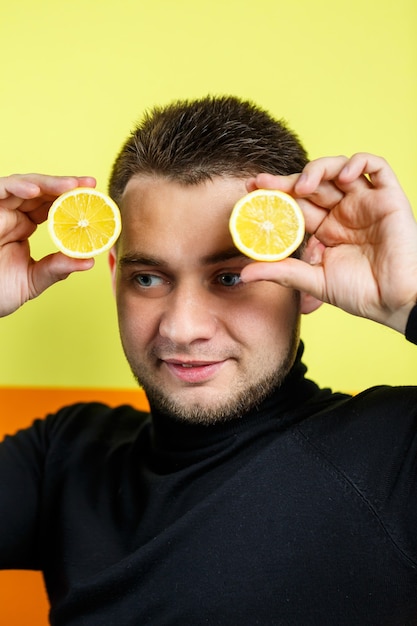 Retrato de un hombre en raglán negro con limón cortado en lugar de ojos. Un tipo con limones cerca de la cara. Una sonrisa en su rostro