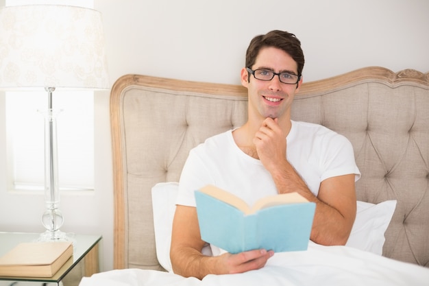 Retrato de hombre relajado leyendo un libro en la cama