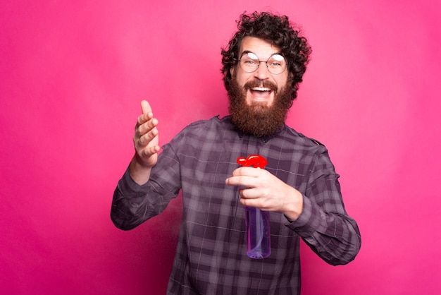 Retrato de hombre rizado y barbudo sonriendo y rociando con desinfectante de manos