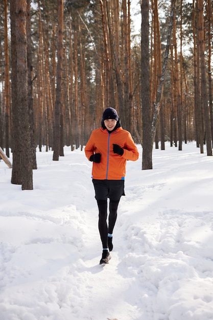 Retrato de un hombre con ropa deportiva brillante corriendo por un bosque de invierno. Día helado