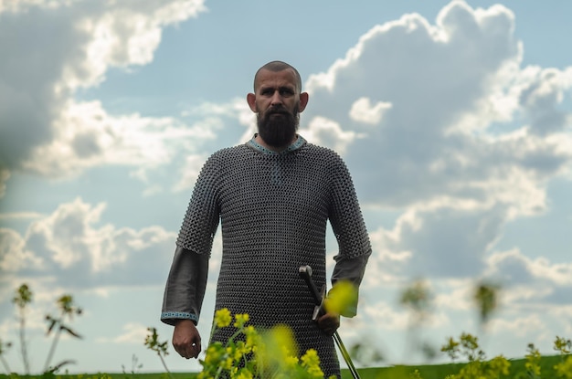 Retrato de hombre con ropa medieval en el campo de verano Armadura vikinga Espada de metal Primer plano