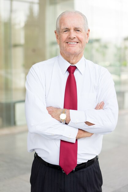 Foto retrato de hombre senior feliz en camisa blanca y corbata con los brazos cruzados.