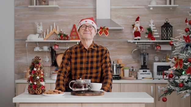 Retrato de hombre senior con gorro de Papá Noel sonriendo mientras mira a la cámara durante la mañana de Navidad