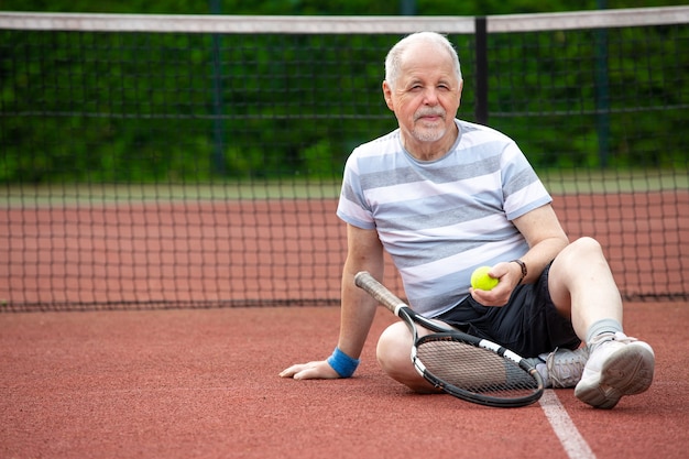 Retrato de hombre senior jugando al tenis en un exterior, deportes jubilados