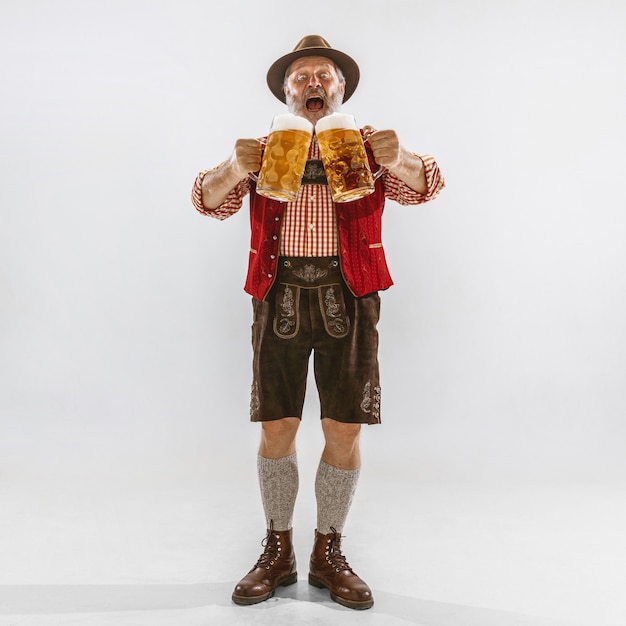 Retrato de hombre senior de Oktoberfest con sombrero, vistiendo la ropa tradicional bávara. Tiro de cuerpo entero masculino en estudio sobre fondo blanco. La celebración, vacaciones, concepto de festival. Invita a la cerveza.