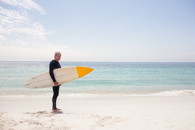 Retrato de hombre senior en traje de neopreno con una tabla de surf