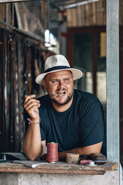 Retrato de un hombre serio y brutal con barba, con sombrero de panamá blanco y negro con un cigarro humeante en los dientes, descansando los codos sobre la mesa. Pasar el concepto de tiempo.