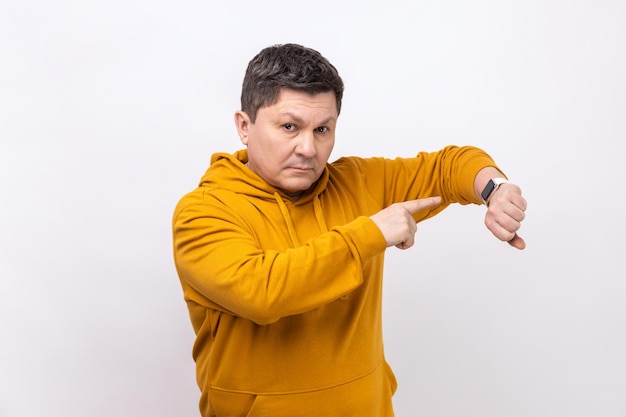 Retrato de un hombre serio y mandón de pie mirando a la cámara y señalando su reloj inteligente