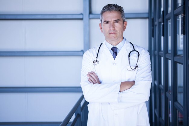 Retrato de hombre serio médico de pie con los brazos cruzados en el hospital