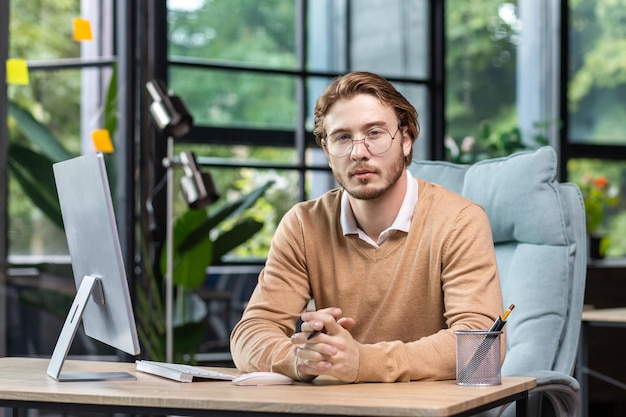 Retrato de hombre serio pensante con computadora dentro de la oficina de loft verde moderno hombre rubio mirando