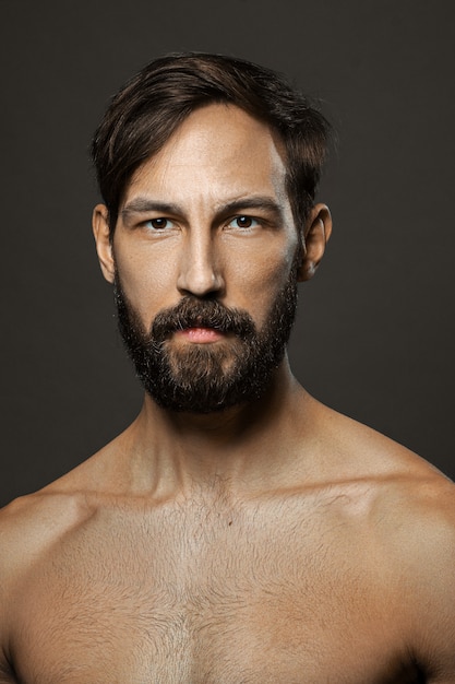 Foto retrato de hombre serio en topless con barba y bigote mirando recto severo.