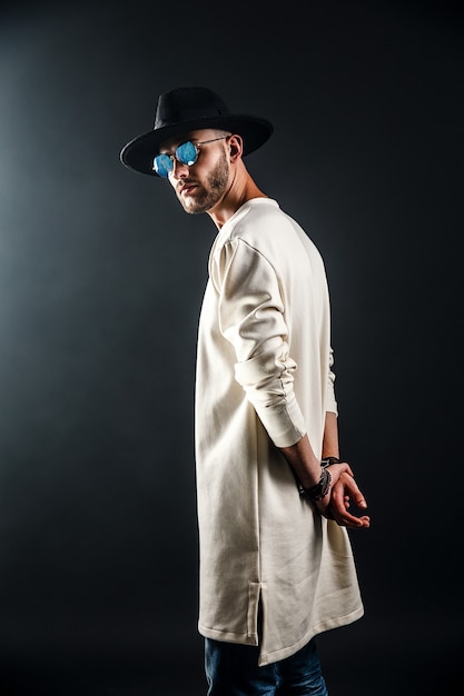 Retrato de un hombre con un sombrero de ala ancha y gafas de sol mirando a la cámara en negro