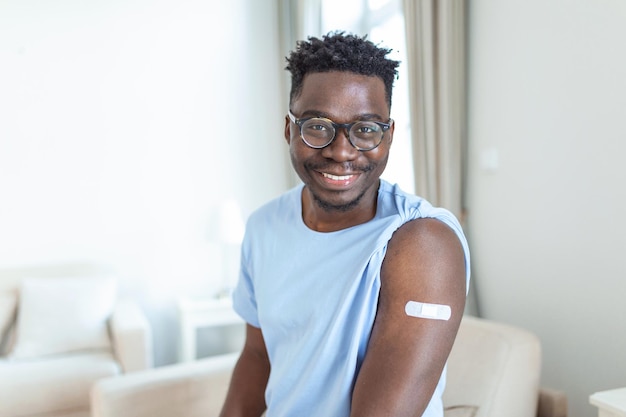 Retrato de un hombre sonriendo después de recibir una vacuna Hombre africano sujetándose la manga de la camisa y mostrando su brazo con una venda después de recibir la vacuna