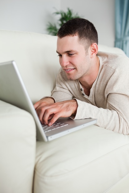 Retrato de un hombre sonriente acostado en un sofá usando una computadora portátil