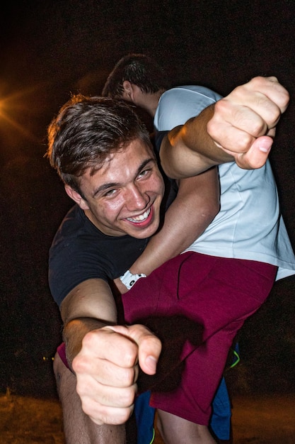 Retrato de un hombre sonriente apretando el puño siendo llevado por un amigo por la noche