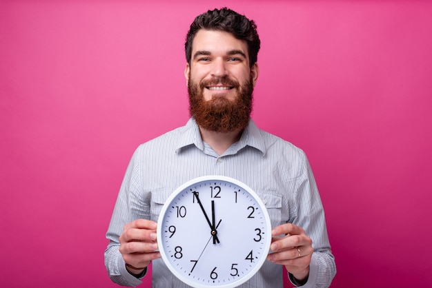 Retrato de hombre sonriente con barba sosteniendo un gran reloj blanco