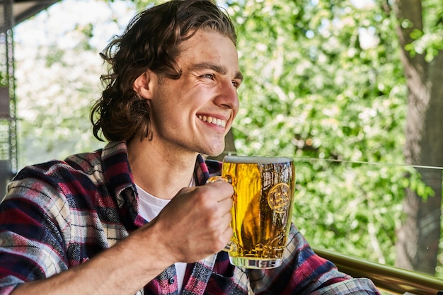 Retrato de hombre sonriente bebiendo cerveza en la cafetería de la terraza de verano.