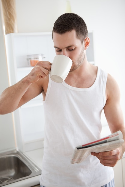 Retrato de un hombre sonriente bebiendo té mientras lee las noticias