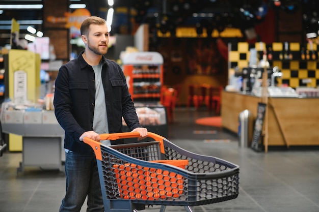 Retrato de un hombre sonriente caminando con su carrito en el pasillo del supermercado