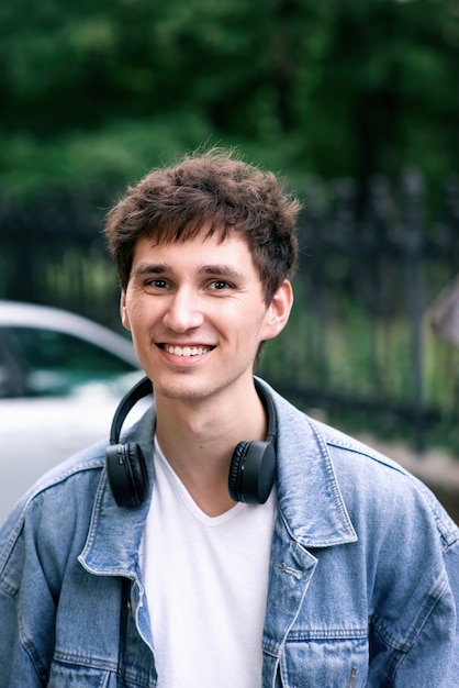Retrato de un hombre sonriente en camiseta blanca y chaqueta de jeans con auriculares