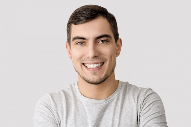 Retrato del hombre sonriente en camiseta gris en el fondo ligero para hacer publicidad