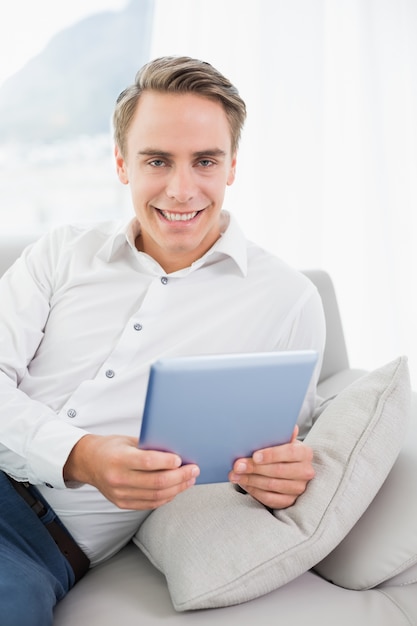 Retrato de un hombre sonriente casual con tableta digital en el sofá