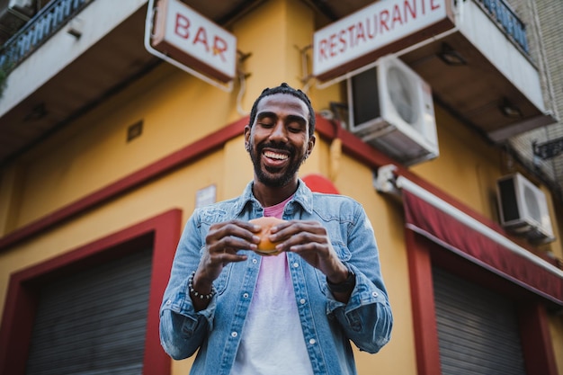 Retrato de un hombre sonriente comiendo comida callejera Está frente a un bar
