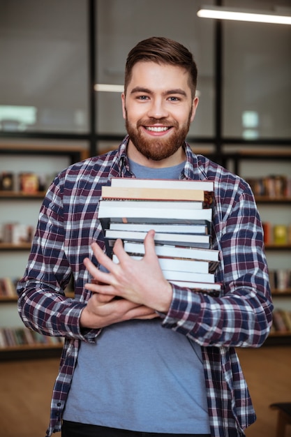 Foto retrato de un hombre sonriente estudiante sosteniendo libros en la biblioteca