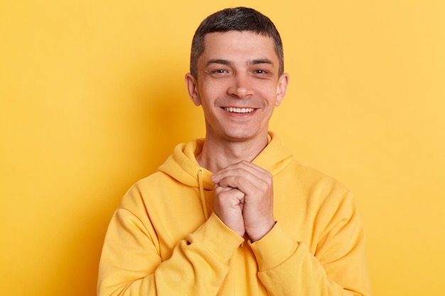 Retrato de un hombre sonriente feliz y satisfecho con una capucha de estilo informal posando aislada sobre un fondo amarillo de pie mirando la cámara expresando felicidad