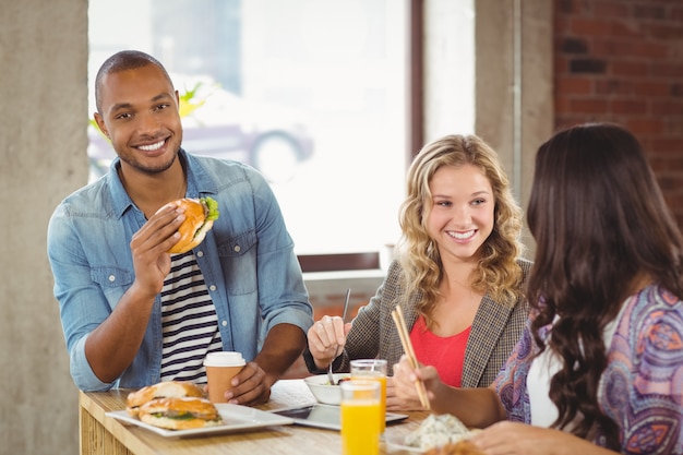 Retrato de hombre sonriente con hamburguesa con colegas