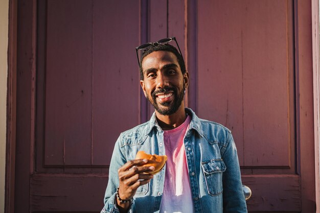 Retrato de un hombre sonriente con una hamburguesa con queso en la calle