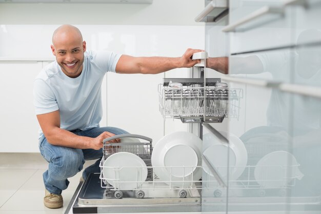 Retrato de hombre sonriente con lavavajillas en la cocina