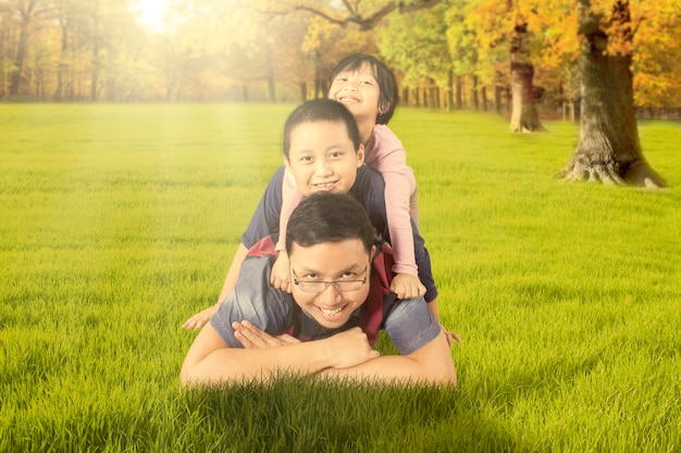 Foto retrato de un hombre sonriente llevando a su hijo e hija en la espalda mientras se acuesta en la hierba