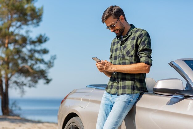 Retrato de hombre sonriente mirando el teléfono al aire libre durante el día