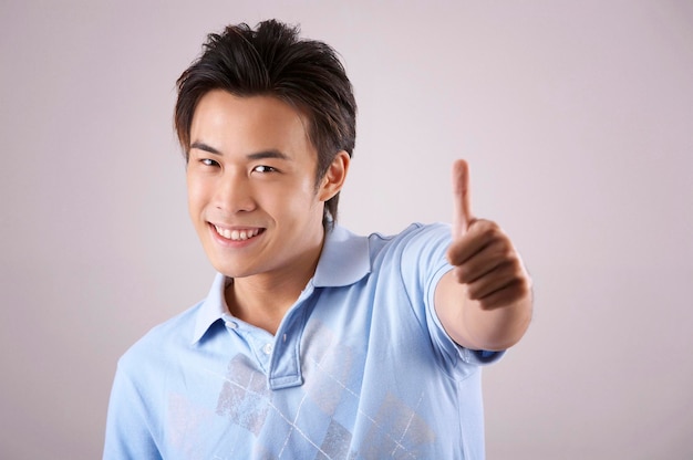 Retrato de un hombre sonriente mostrando el pulgar hacia arriba contra un fondo gris