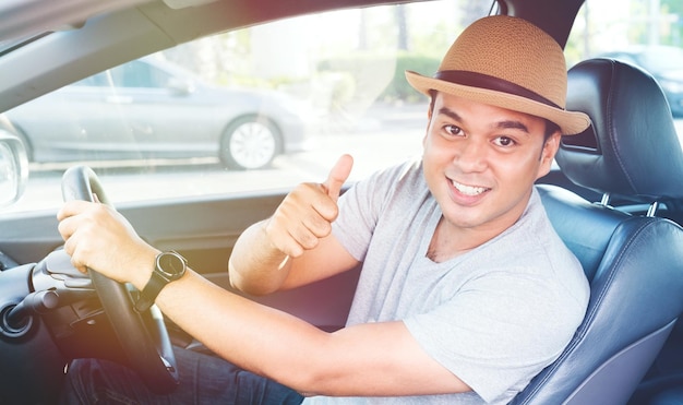 Retrato de un hombre sonriente mostrando los pulgares hacia arriba mientras está sentado en el coche