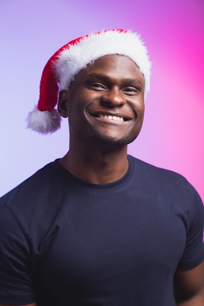 Retrato de hombre sonriente positivo con gorro de Papá Noel y camiseta casual sobre fondo de colores, tiempo de Navidad. Vacaciones de invierno y concepto de personas emocionales.