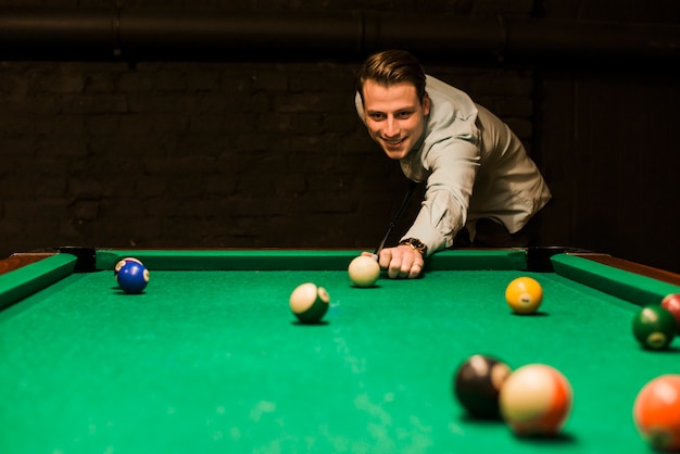 Foto retrato de un hombre sonriente que apunta la bola de señal mientras juega al billar